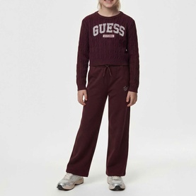 Model wearing burgundy Guess cable-knit sweater and wide-leg joggers with logo branding, styled with white trainers