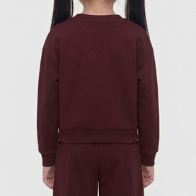 Model wearing Guess Deep Maroon children's sweat top, shown from behind, styled with matching maroon joggers.