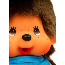 Monchhichi blue plush soft toy close-up showing friendly orange face with freckles, dark eyes, red open mouth, and brown fluffy hair.