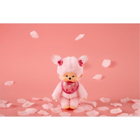 Monchhichi pink plush soft toy with floral hair accessories and pink bib, surrounded by scattered pink petals on pink background