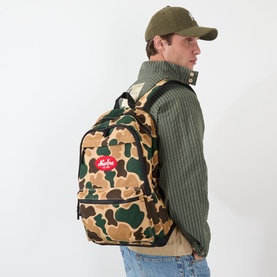 Model carrying New Era Delaware Light Camo Backpack in multi camo print with red Heritage Script logo patch and padded shoulder straps.