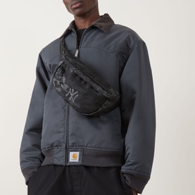 Model carrying New Era New York Yankees MLB Camo Belt Bag in black camo, worn across chest, with grey Carhartt zip-up jacket.