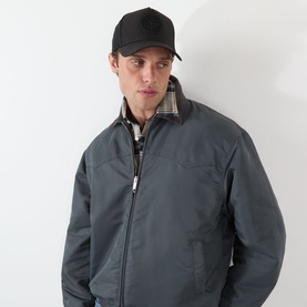 Model with New Era Seattle Mariners MLB Sport 9FORTY Trucker Cap in black, worn with a grey zip-up jacket with plaid collar lining.