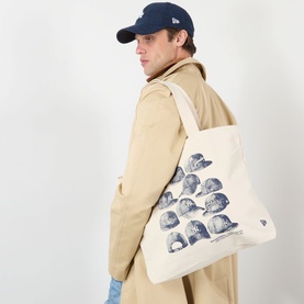 Model carrying New Era New York Yankees MLB Cap Graphic Tote Bag in beige canvas, navy cap array graphic, styled with beige trench coat and navy cap.