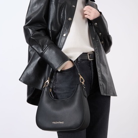 Model carrying Mario Valentino Brixton Logo Shoulder Bag in Nero with gold-tone hardware, styled with black leather jacket and jeans.