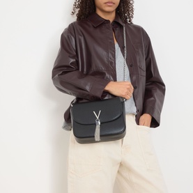 Model carrying Mario Valentino Divina Top Handle Crossbody Bag in black with silver-tone hardware and V-logo tassel detail, styled with dark leather