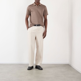 Model wearing taupe short-sleeve polo shirt and cream wide-leg trousers, styled with a black belt and black loafers