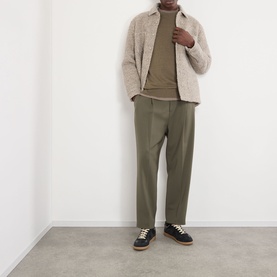 Model wearing NN07 Ted Linen Knitted Sweater in Capers, styled with a textured zip jacket, olive trousers and dark trainers.