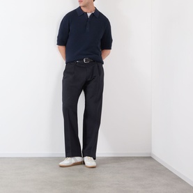 Model wearing NN07 Kay Relaxed Fit Pleated Trousers in navy blue with double front pleats, styled with a navy polo shirt and white trainers.