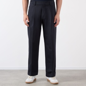 Model wearing NN07 Kay Relaxed Fit Pleated Trousers in navy blue, double front pleats, styled with white trainers.