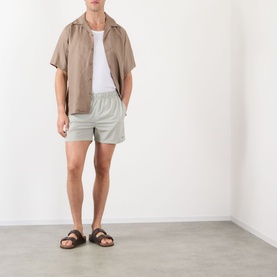 Model wearing NN07 Green Stripe shorts with a beige short-sleeve shirt, white T-shirt, and brown leather sandals.