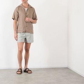Model wearing NN07 Green Stripe shorts, styled with a taupe short-sleeve shirt and brown leather sandals.