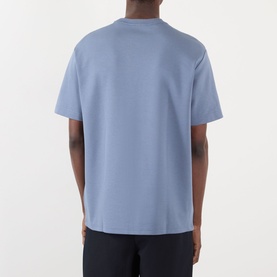 Back view of model wearing a pale blue oversized crew neck T-shirt with short sleeves, styled with dark navy trousers.