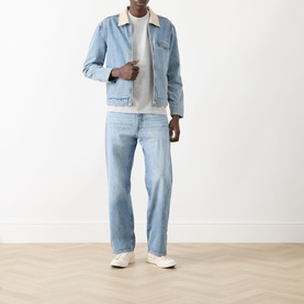 Model wearing Paige Laughlin Acid Wash Denim Jacket in Moby, light blue with cream collar, styled with matching denim jeans and white trainers.