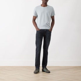 Model wearing Paige Sorden Solid T-Shirt in Bristol Blue with dark wash jeans and grey suede shoes.