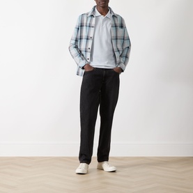 Model wearing Paige Demille Solid Polo Shirt in Bristol Blue Combo, styled with plaid overshirt, black jeans and white trainers.