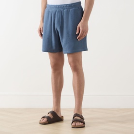 Model wearing Paige Elijah Hidden Drawstring Shorts in Lakeside blue pebbled loop knit fabric, styled with brown leather sandals.