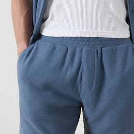 Model wearing Paige Elijah Hidden Drawstring Shorts in Lakeside blue, elasticated waistband visible, styled with white ribbed top.