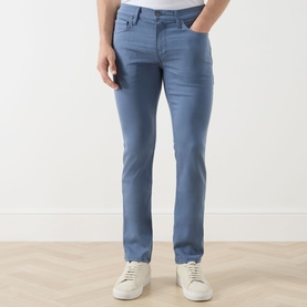 Model wearing Paige Slim Jeans in Flint Stone, styled with white trainers. Five-pocket design in a mid-blue washed finish.