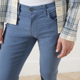 Model wearing Paige Flint Stone slim jeans in blue-grey, styled with a plaid shirt. Five-pocket design, slim fit.