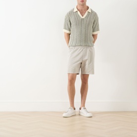 Model wearing Paige Shallow shorts in light beige, styled with a grey cable-knit polo shirt and white trainers.