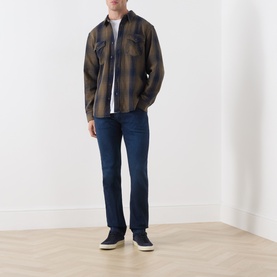 Model wearing Paige Pembry straight jeans in dark indigo, styled with a brown plaid overshirt, white tee and navy trainers.