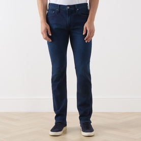 Model wearing Paige Straight Jeans in Pembry dark blue denim, styled with white trainers and grey top.