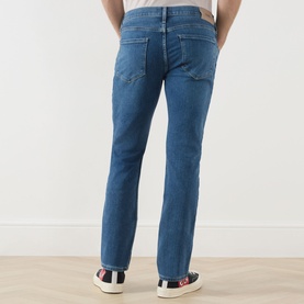 Model wearing Paige straight jeans in Bushman blue denim, rear view, styled with white tee and multicolour trainers