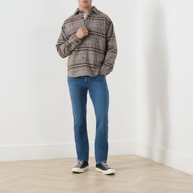 Model wearing Paige Bushman straight jeans in mid-blue wash, styled with a brown check overshirt and black trainers.