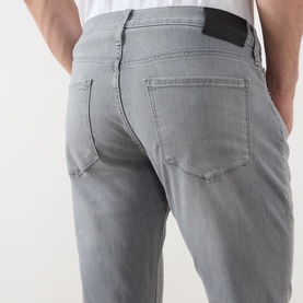 Model wearing Paige Wainwright straight jeans in grey, rear view showing back pockets and black branded patch at waistband.
