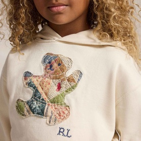 Model wearing Ralph Lauren Patchwork Polo Bear Logo Terry Hoodie in Guide Cream with patchwork bear appliqu&eacute; and RL embroidery.