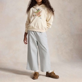 Model wearing Ralph Lauren Patchwork Polo Bear Logo Terry Hoodie in Guide Cream with blue striped wide-leg trousers and brown loafers.