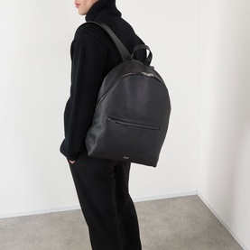 Model carrying Tom Ford Foil Logo Grained Leather Backpack in black with silver-tone logo detail, styled with all-black outfit