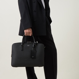 Model carrying Tom Ford Elliot Leather Briefcase in Navy Black, pebbled calf leather with dual top handles and embossed logo, styled with black suit