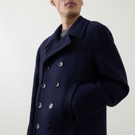 Model wearing Tom Ford navy wool coat, double-breasted with dark buttons, close-up detail view showing lapel and chest pockets.