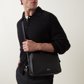 Model carrying Tom Ford black leather crossbody bag with silver-tone hardware and adjustable shoulder strap, styled with black jacket