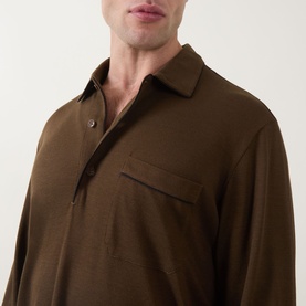 Model wearing Tom Ford brown silk-cotton polo shirt, showing spread collar, chest pocket, and long sleeves in close-up detail shot.