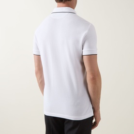 Model wearing Tom Ford white and black polo shirt, rear view, with contrast tipped collar and sleeves, paired with black trousers.