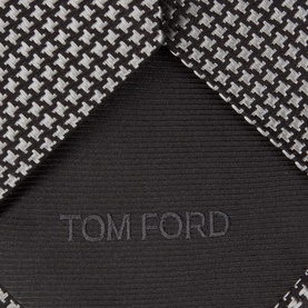 Tom Ford grey silk tie in houndstooth pattern with embossed logo detail, shown folded to highlight texture and branding.