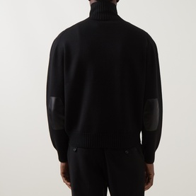 Model wearing Tom Ford black virgin wool zip-through jumper, rear view, with leather elbow patches and ribbed cuffs.