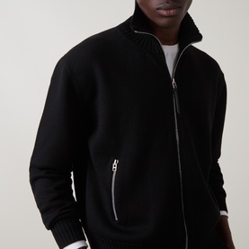 Model wearing Tom Ford black virgin wool zip-through knit jacket with silver zip detail and leather patch pockets, styled over white T-shirt.