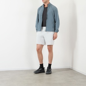 Model wearing 247 Dusky Navy casual nylon jacket with white shorts and black trainers.
