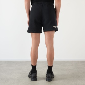 Model wearing 247 Jet Black cotton shorts with small logo print, styled with black trainers, rear view