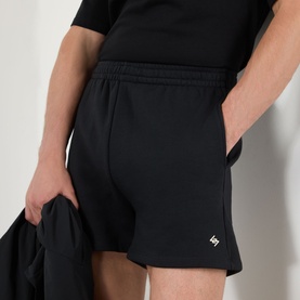 Model wearing 247 Jet Black cotton shorts with elasticated waist and small logo detail, styled with matching black T-shirt
