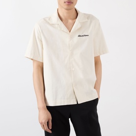 Model wearing Almost Home Logo Bowling Shirt in Cloudskin, with notched lapels, short sleeves and embroidered chest logo, styled with black trousers.