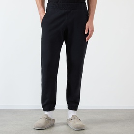 Model wearing Almost Home Workwear Logo Sweatpants in Porto Black, tapered leg with cuffed ankles, styled with grey slip-on sandals