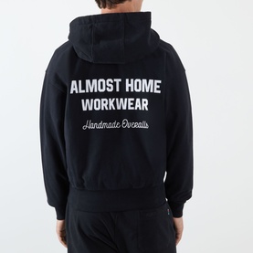 Model wearing Almost Home Workwear Logo Zip Hoodie in Porto Black, rear view showing enlarged contrast logo lettering, paired with matching black