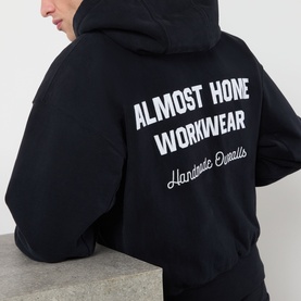 Model wearing Almost Home Workwear Logo Zip Hoodie in Porto Black, back view showing enlarged contrast white logo lettering print.