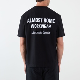 Model wearing Almost Home Workwear Logo T-Shirt in Porto Black, showing back with enlarged white logo lettering and script detail.