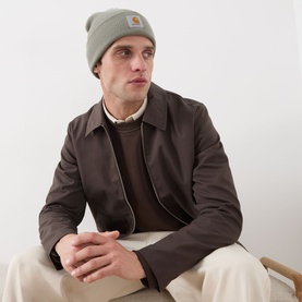 Model with Carhartt Watch Logo Beanie in Shady Green, ribbed knit with turned-up brim, styled with dark brown jacket and brown knitwear